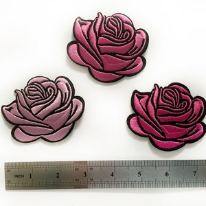 May include: Three pink embroidered rose patches with black outlines. The patches are approximately 5 cm in diameter. A ruler is included for size reference.