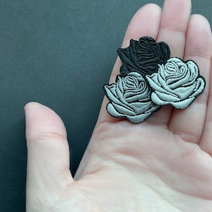Könnte beinhalten: Drei gestickte Bügelbilder in Form von Rosen. Eine Rose ist schwarz und die anderen beiden sind silber.