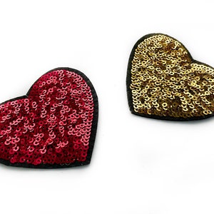 Könnte beinhalten: Zwei herzförmige Patches, einer rot und einer gold, mit Pailletten besetzt.