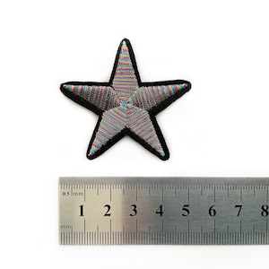 May include: A colorful, striped, five-pointed star-shaped patch with a black outline. The patch is approximately 4 cm wide.