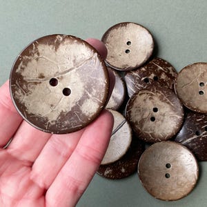 Peut inclure: Un ensemble de gros boutons ronds en noix de coco. Les boutons, de couleur marron et beige, sont percés de deux trous pour la couture. L'aspect naturel et texturé de ces boutons est idéal pour divers projets de couture. Mesurent environ 4 cm de diamètre.