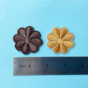 May include: Two embroidered flower patches, one brown and one gold, measuring approximately 2.5 cm in diameter. The patches are shown next to a ruler for size reference.
