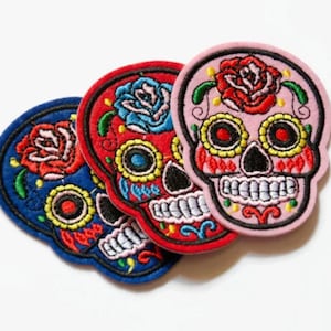 Könnte beinhalten: Drei gestickte Zucker Schädel Patches in Pink, Rot und Blau mit floralen Designs.