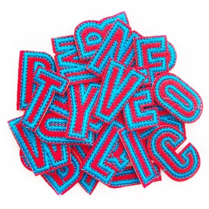 May include: A pile of red felt letters with blue stitching. The letters are all uppercase and are in a variety of fonts.