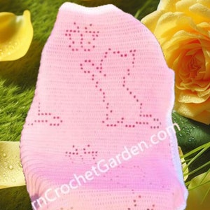 May include: A pink crocheted baby blanket with a white border and a floral design. The blanket is on a chair with a yellow rose and rose petals in the background.