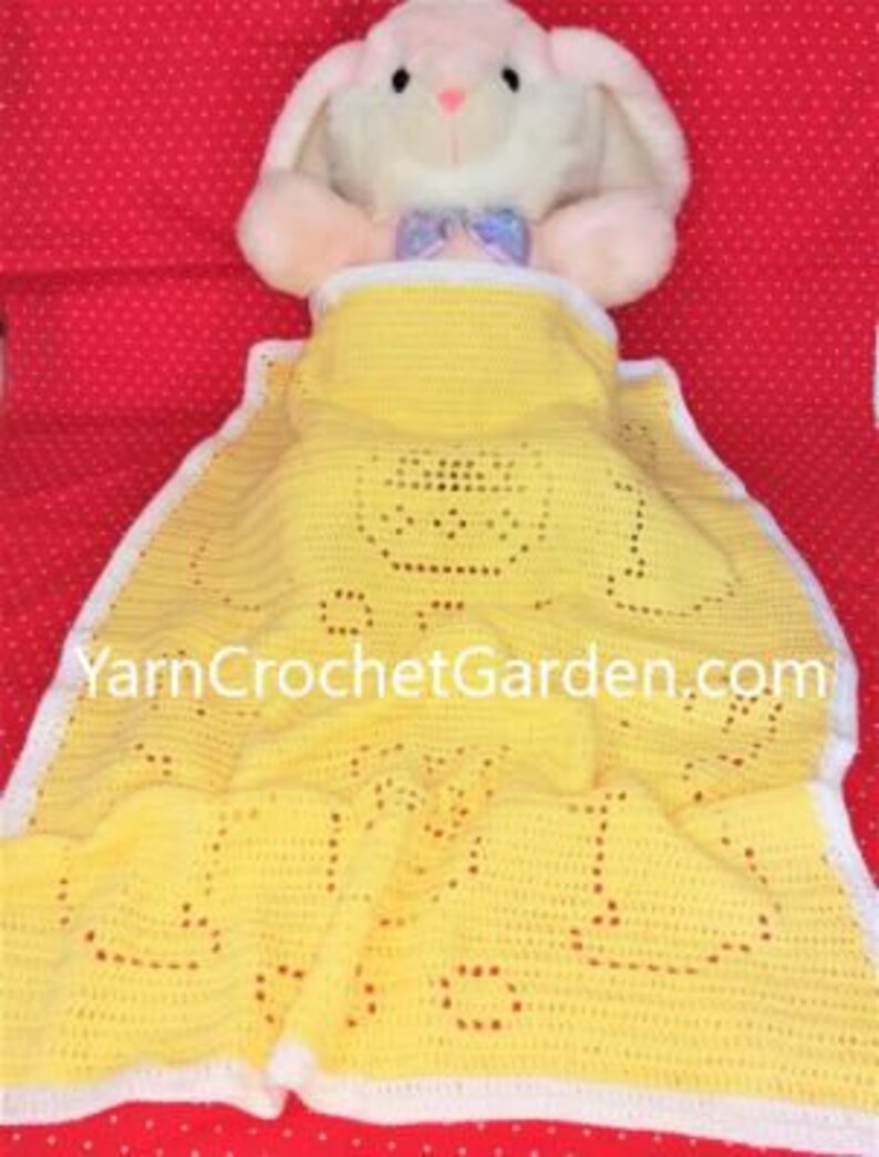 May include: A yellow crocheted baby blanket with a white border. The blanket has a crocheted design of a bunny rabbit. The blanket is lying on a red surface with white polka dots. The text "YarnCrochetGarden.com" is visible on the blanket.