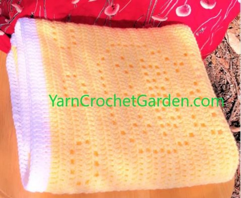 May include: A yellow crochet baby blanket with a white border. The blanket has a delicate, lacy pattern and is made with soft yarn. YarnCrochetGarden.com