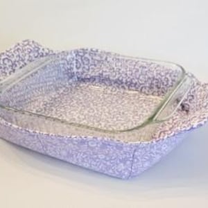 May include: A purple and white floral patterned fabric baking dish holder. The holder is made of fabric and has a quilted design. The holder is designed to fit a standard size baking dish.