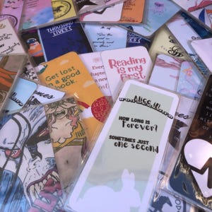 Könnte beinhalten: Eine Sammlung bunter Lesezeichen mit verschiedenen Designs und Zitaten. Einige Lesezeichen zeigen Illustrationen von Tieren, Blumen und abstrakten Mustern. Andere haben Text wie "Verliere dich in einem guten Buch" und "Lesen ist meine erste Liebe".