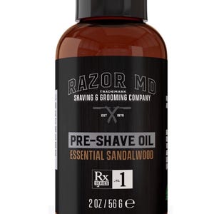 May include: A brown bottle of Razor MD pre-shave oil with a black cap. The label reads "PRE-SHAVE OIL ESSENTIAL SANDALWOOD" and "2 OZ / 56 g". The brand name "RAZOR MD" is at the top.