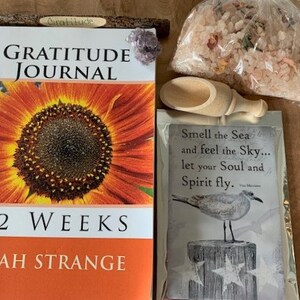 May include: A gratitude journal with a sunflower on the cover, a wooden pencil, a small bag of bath salts, a wooden scoop, and a card with the text "Smell the Sea and feel the Sky... let your Soul and Spirit fly."