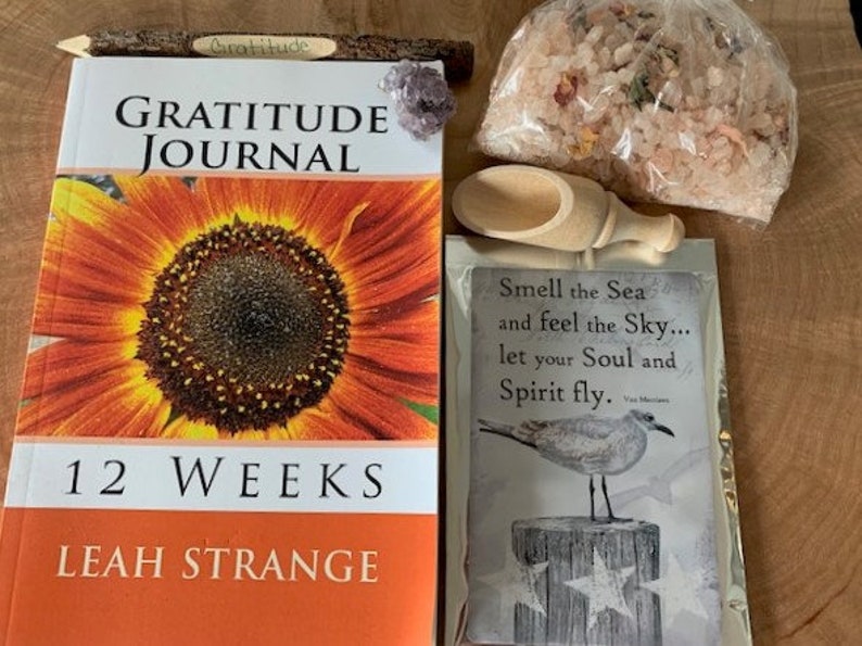 May include: A gratitude journal with a sunflower on the cover, a wooden pencil, a small bag of bath salts, a wooden scoop, and a card with the text "Smell the Sea and feel the Sky... let your Soul and Spirit fly."