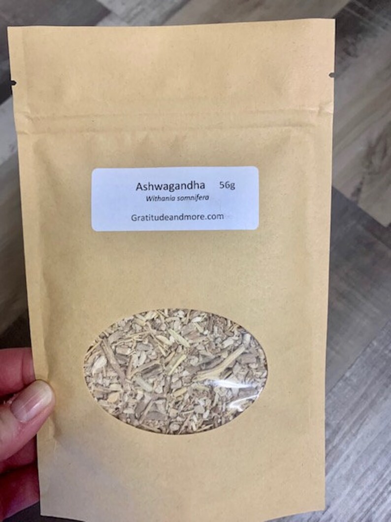 May include: A brown paper bag with a white label that reads "Ashwagandha 56g Withania somnifera Gratitudeandmore.com". The bag contains dried herbs.