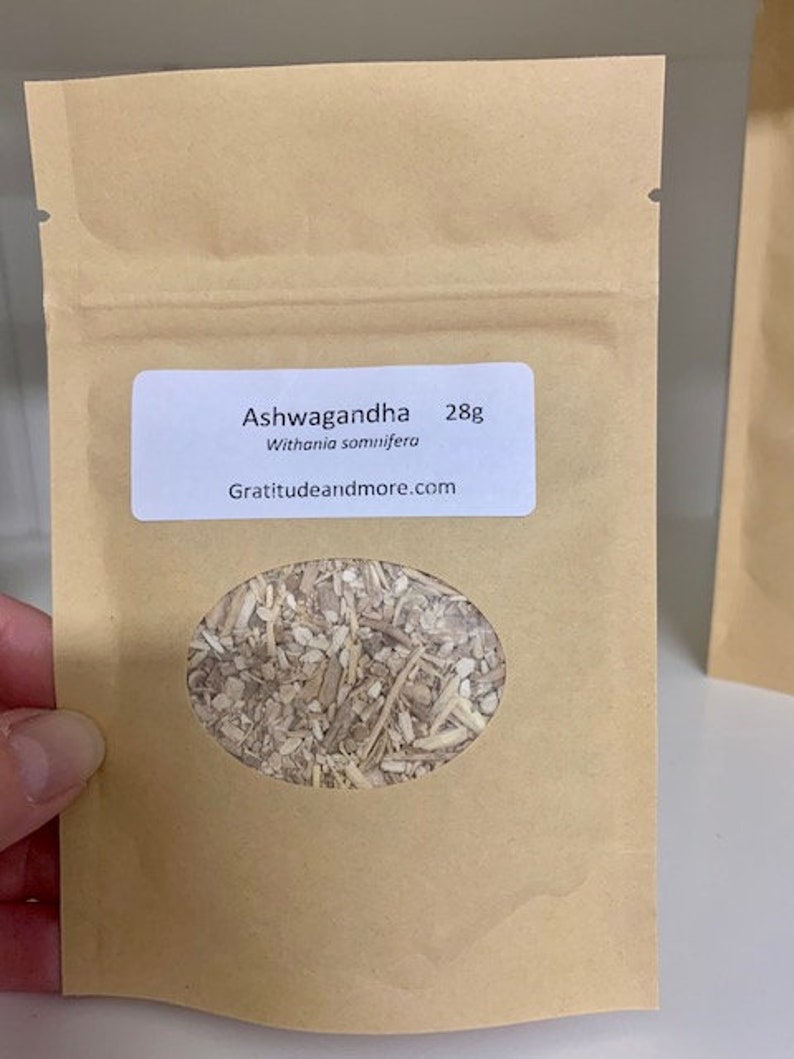 May include: A brown paper bag with a white label that reads "Ashwagandha 28g Withania somnifera Gratitudeandmore.com". The bag has a clear window showing dried herbs inside.