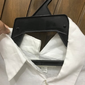 Puede incluir: Camisa blanca de lino con cuello abotonado y una etiqueta que dice "Comme des Gar&ccedil;ons" y "Jap&oacute;n".