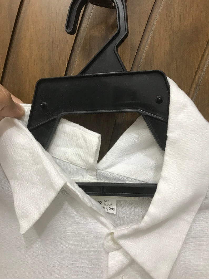 Puede incluir: Camisa blanca de lino con cuello abotonado y una etiqueta que dice "Comme des Gar&ccedil;ons" y "Jap&oacute;n".