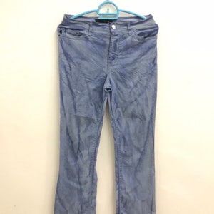 Puede incluir: Un pantalón de pana azul claro colgado de una percha azul sobre un fondo blanco.