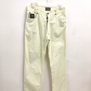 May include: A pair of off-white cotton pants with a button fly and a small pocket on the right side. The pants have the text "VERSACE JEANS" on the back waistband.