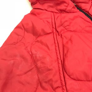 May include: Red quilted jacket with a zipper closure. The jacket has a hood and is made of a lightweight material.