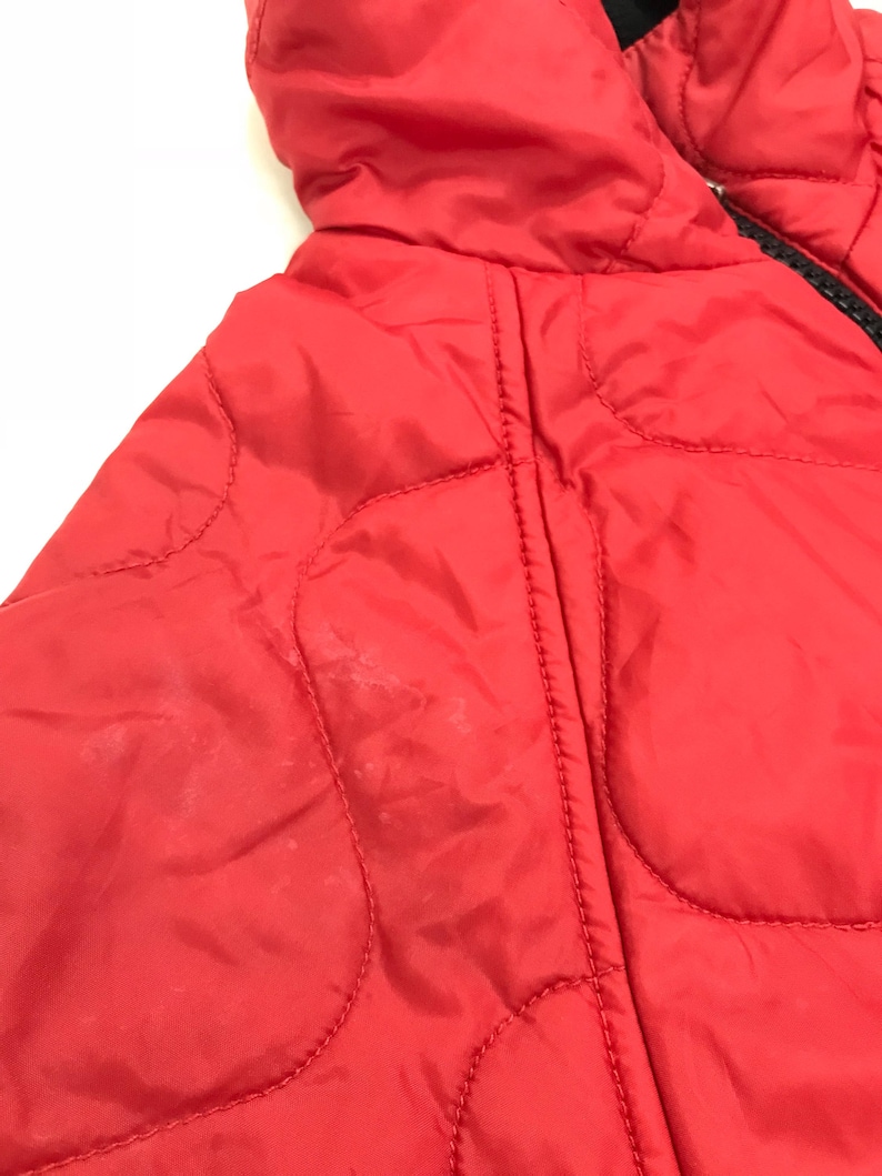 May include: Red quilted jacket with a zipper closure. The jacket has a hood and is made of a lightweight material.