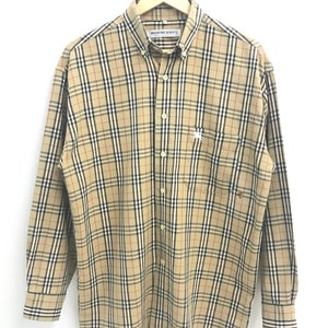 May include: A long-sleeved button-down shirt with a brown, black, and red plaid pattern. The shirt has a small embroidered logo on the left chest pocket. The label reads "Burberry's".