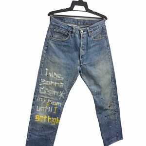 May include: Blue denim jeans with paint splatters and white and yellow writing on the left leg. The writing says "I was born different my room until I got high".