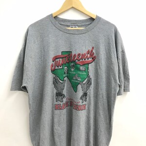 May include: Gray t-shirt with a graphic of a red and green outline of Texas with the word "Juneteenth" in red lettering. The graphic also includes a depiction of hands holding the state, with the text "Celebration of Black Freedom" below.