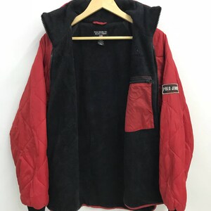 May include: Red quilted jacket with a black fleece lining and a zipper closure. The jacket has a small pocket on the left side and a Polo Jeans label on the right side.
