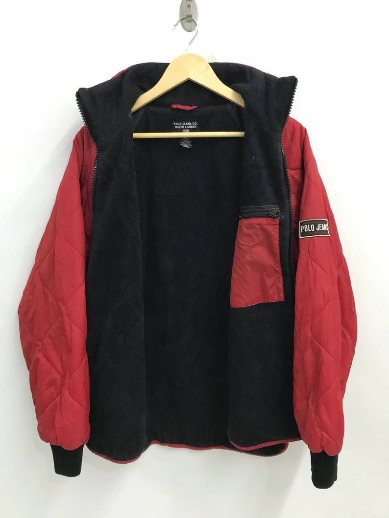 May include: Red quilted jacket with a black fleece lining and a zipper closure. The jacket has a small pocket on the left side and a Polo Jeans label on the right side.