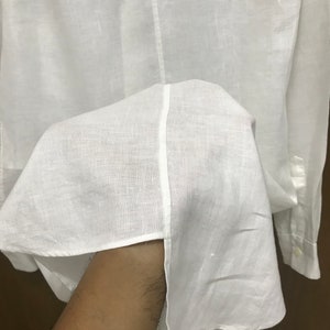 Puede incluir: Camisa blanca de lino con mangas largas y cierre de botones.
