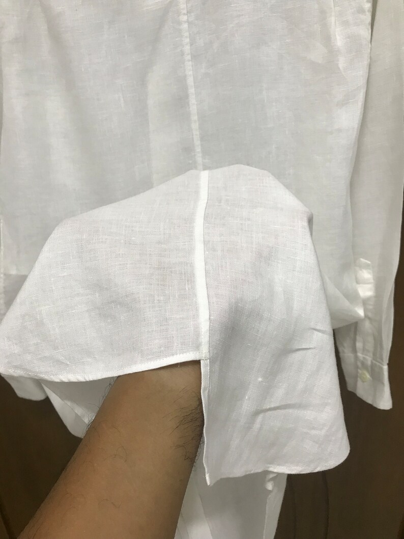 Puede incluir: Camisa blanca de lino con mangas largas y cierre de botones.