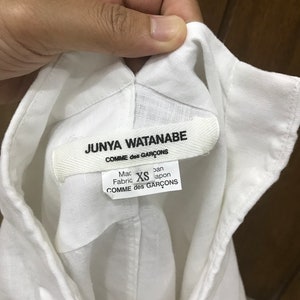 Puede incluir: Camisa blanca de lino con una etiqueta de Junya Watanabe Comme des Gar&ccedil;ons. La etiqueta dice "Hecho en Jap&oacute;n" y "Tejido: XS".