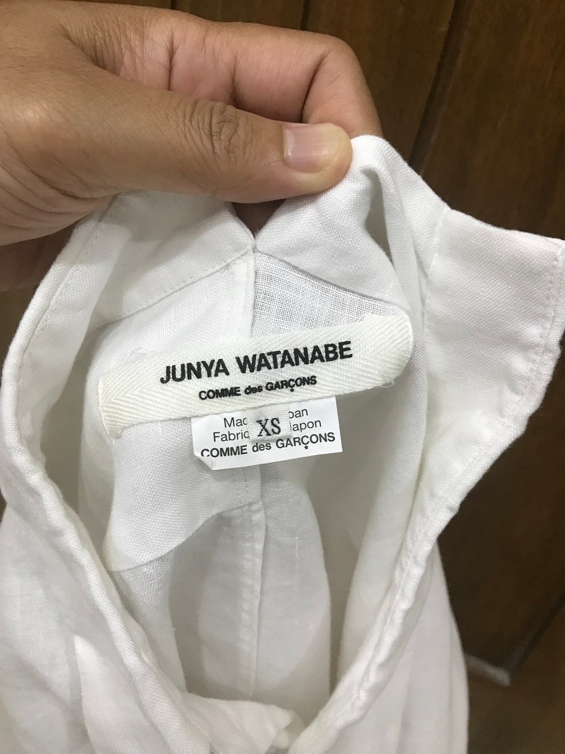 Puede incluir: Camisa blanca de lino con una etiqueta de Junya Watanabe Comme des Gar&ccedil;ons. La etiqueta dice "Hecho en Jap&oacute;n" y "Tejido: XS".