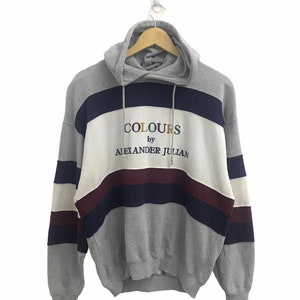 Könnte beinhalten: Grauer Kapuzenpullover mit mehrfarbigem Streifenmuster und "COLOURS by ALEXANDER JULIAN" Stickerei auf der Vorderseite.