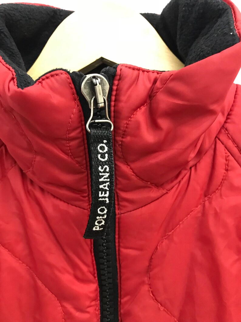 May include: Red quilted jacket with a black zipper and a black "POLO JEANS CO." label on the zipper pull.
