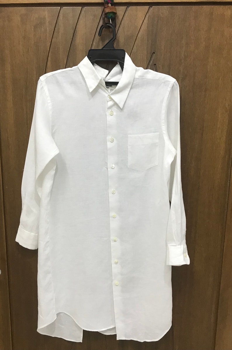 Puede incluir: Una camisa blanca de lino de manga larga con cuello abotonado y un solo bolsillo en el pecho izquierdo. La camisa tiene un dobladillo curvo.