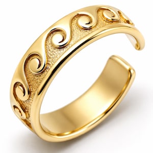 Puede incluir: Un anillo abierto de color dorado que presenta un patrón de ondas en relieve continuo a lo largo de la banda exterior. La superficie del anillo muestra un acabado pulido en los diseños de ondas elevadas, contrastado con un fondo mate texturizado.