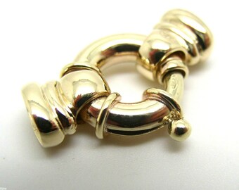 Pode incluir: Um fecho de metal dourado com um anel redondo e um design decorativo. O fecho é feito de metal polido e tem um acabamento liso e brilhante.