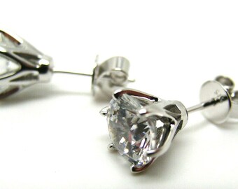 May include: A pair of silver stud earrings with clear cubic zirconia stones. The stones are set in a prong setting and have a round shape.