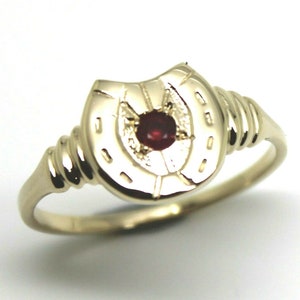 Puede incluir: Un anillo de oro con un diseño de herradura y una piedra preciosa roja en el centro.