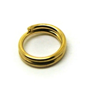 Puede incluir: Un anillo de salto de metal dorado, un tipo de hallazgo de joyería, con un acabado liso y pulido.