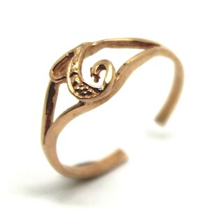 Puede incluir: Un anillo de dedo del pie de color dorado con un diseño delicado y en espiral.