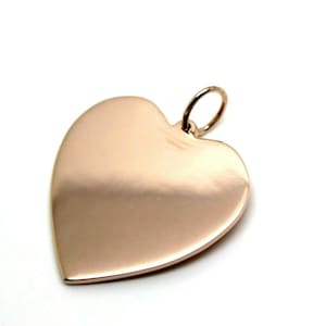 Könnte beinhalten: Ein herzförmiger Anhänger aus Roségold mit glatter, polierter Oberfläche. Der Anhänger hat oben eine kleine Öse zum Anbringen an einer Kette oder Schnur.