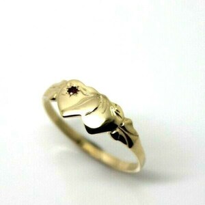 Puede incluir: Un anillo de oro con un diseño en forma de corazón y una pequeña piedra preciosa roja en el centro.