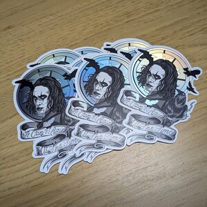 May include: Five silver holographic stickers featuring a black and white illustration of a man with long black hair and a clock behind him. The text on the sticker reads "It Can't Rain All The Time".