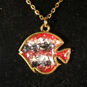 May include: A gold chain necklace with a red and silver glitter fish pendant.