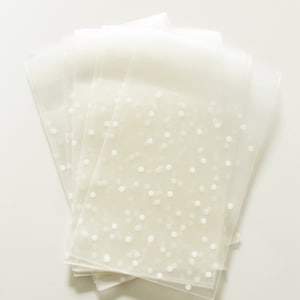 Puede incluir: Un montón de bolsas de regalo de plástico transparente con un patrón de lunares blancos.