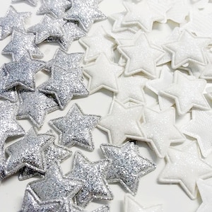 Può includere: Un assortimento di decorazioni a forma di stella in glitter argento e bianco. Le stelle argentate hanno una texture scintillante, mentre le stelle bianche hanno un aspetto liscio e leggermente strutturato. Queste stelle decorative sono ideali per l'artigianato e gli abbellimenti.