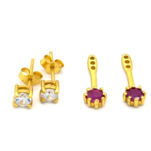 May include: A pair of gold earrings with a clear stone and a pair of gold earrings with a purple stone.