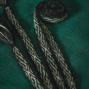 May include: Three black and white braided cords with a diamond pattern on a dark green fabric background. The word "Hornir" is written in white script at the top of the image.
